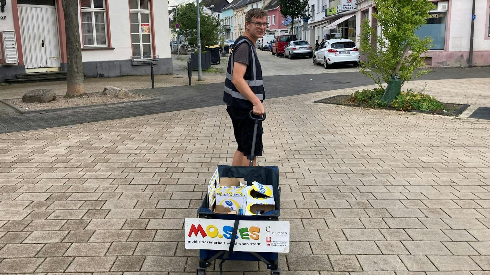 Ein Mann zieht einen Bollerwagen durch eine Innenstadt.