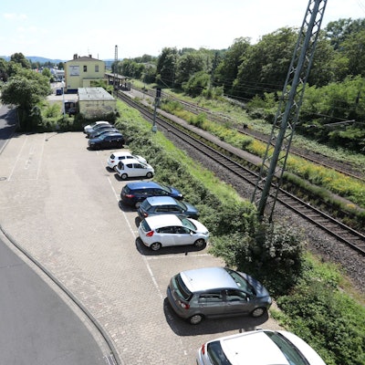 Blick von einer Brücke auf einen Parkplatz, im Hintergrund das Bahnhofsgebäude.