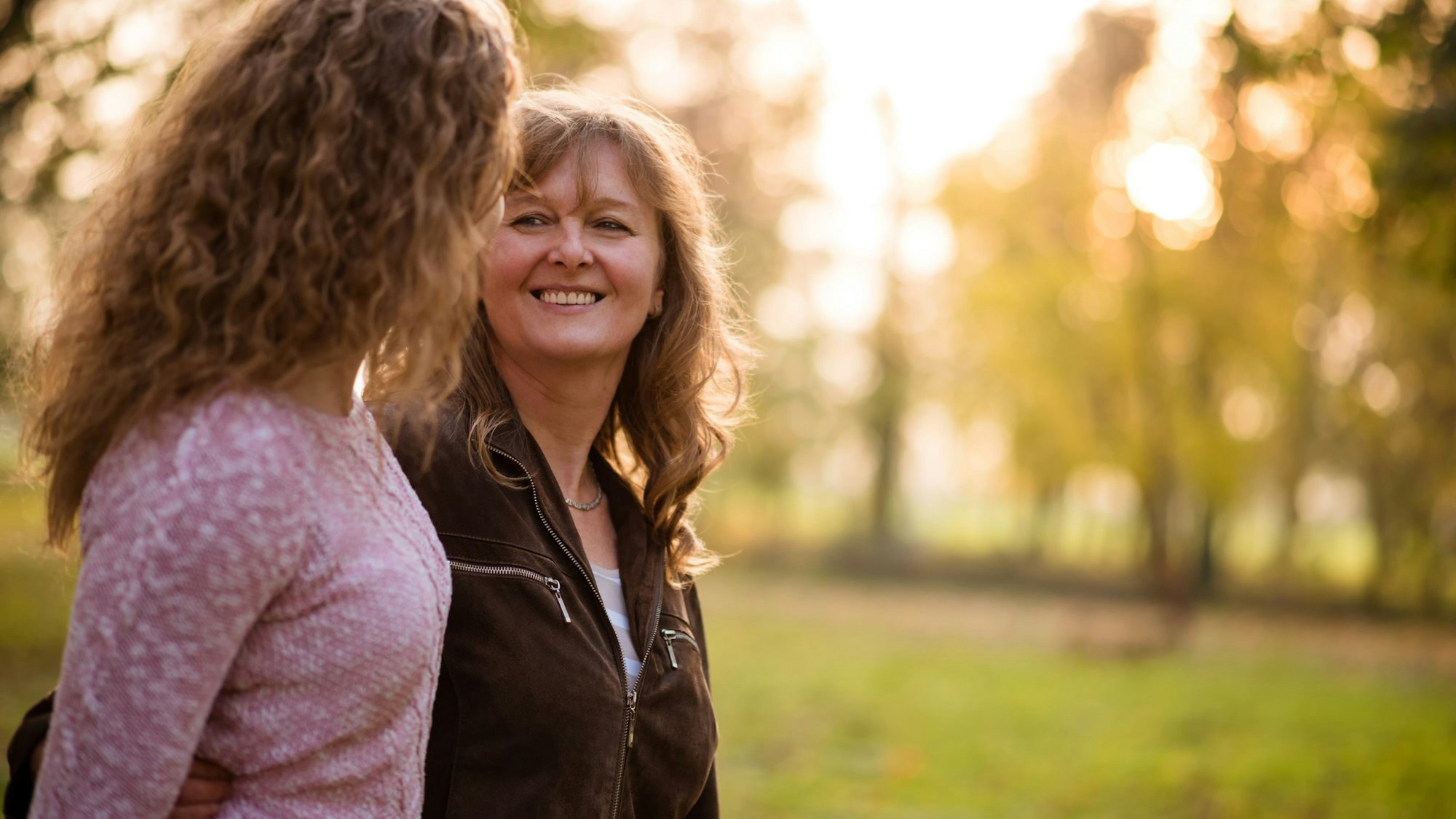 Zwei Frauen schauen sich beim Spazierengehen lächelnd an