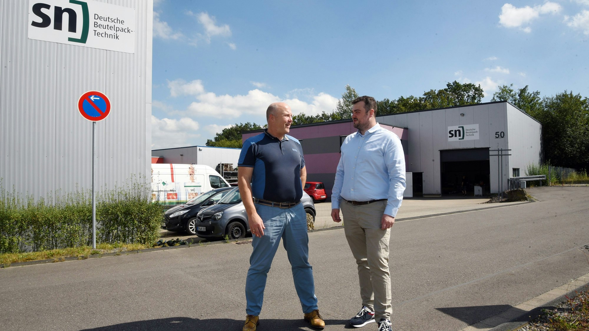 Das Foto zeigt zwei Männer und im Hintergrund zwei Hallen der Firma SN.