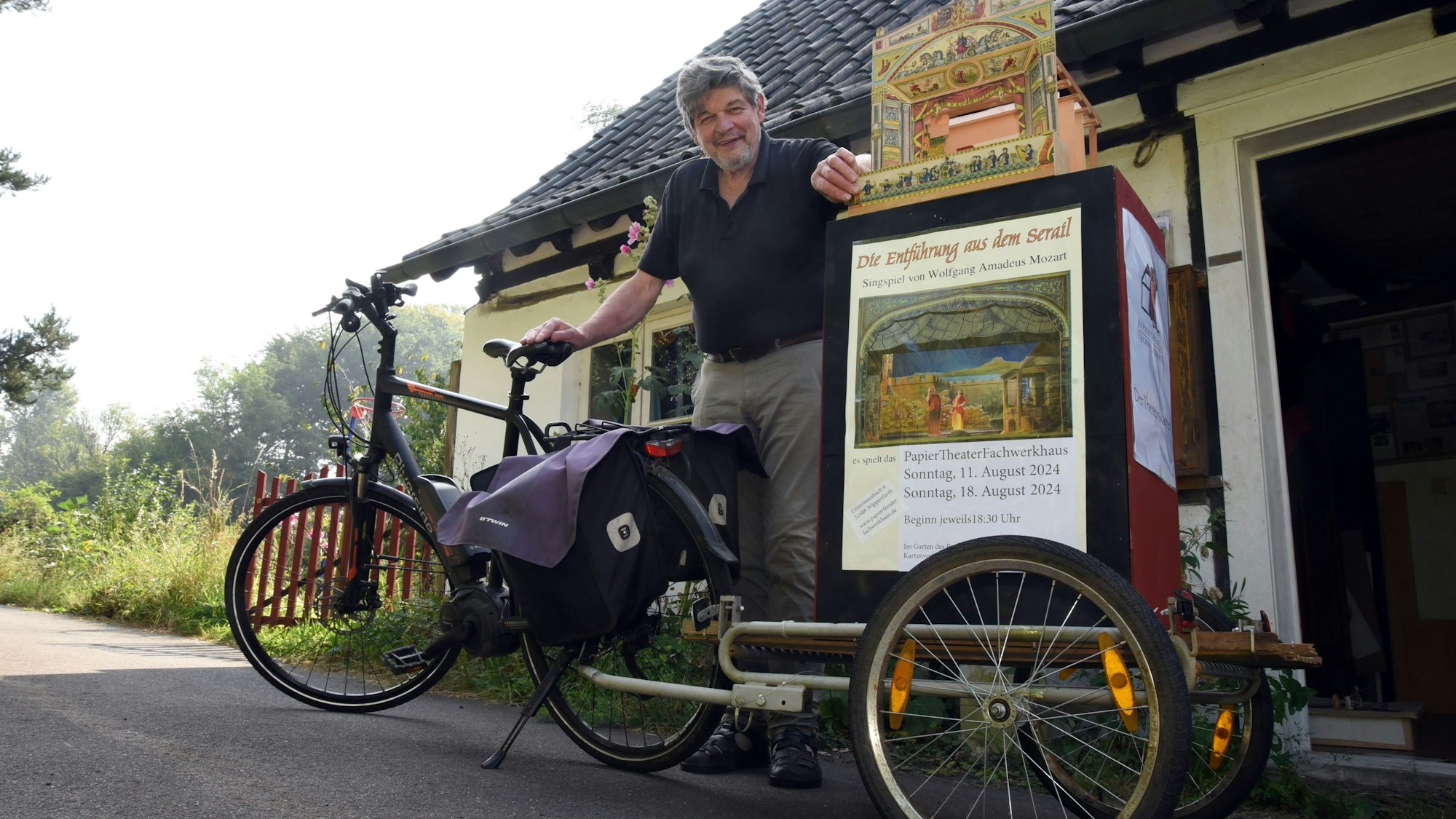 Das Foto zeigt ein Fahrrad mitsamt Anhänger, auf dem ein Papiertheater steht. Hinter dem Fahrrad steht Peter Schauerte-Lüke.