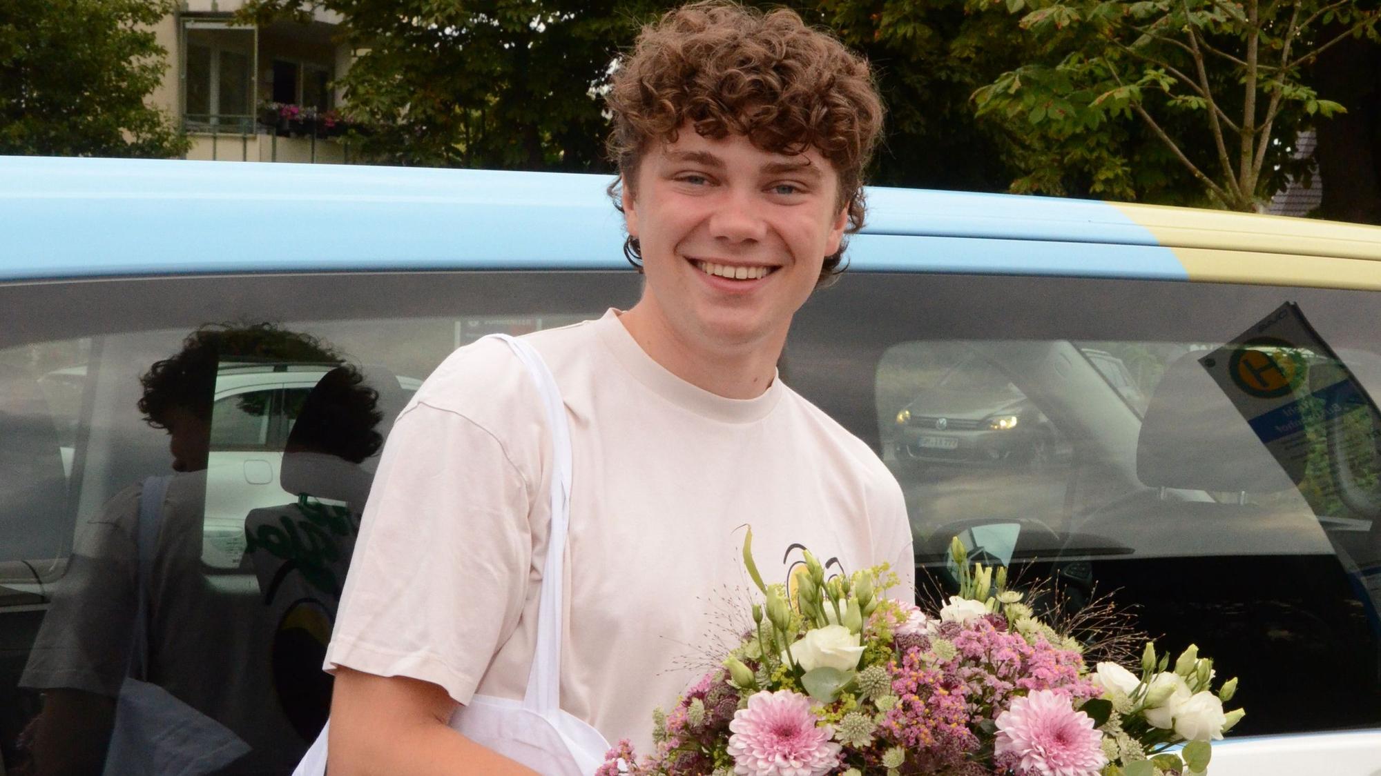 Zu sehen ist ein junger Mann mit einem Blumenstrauß in der Hand.