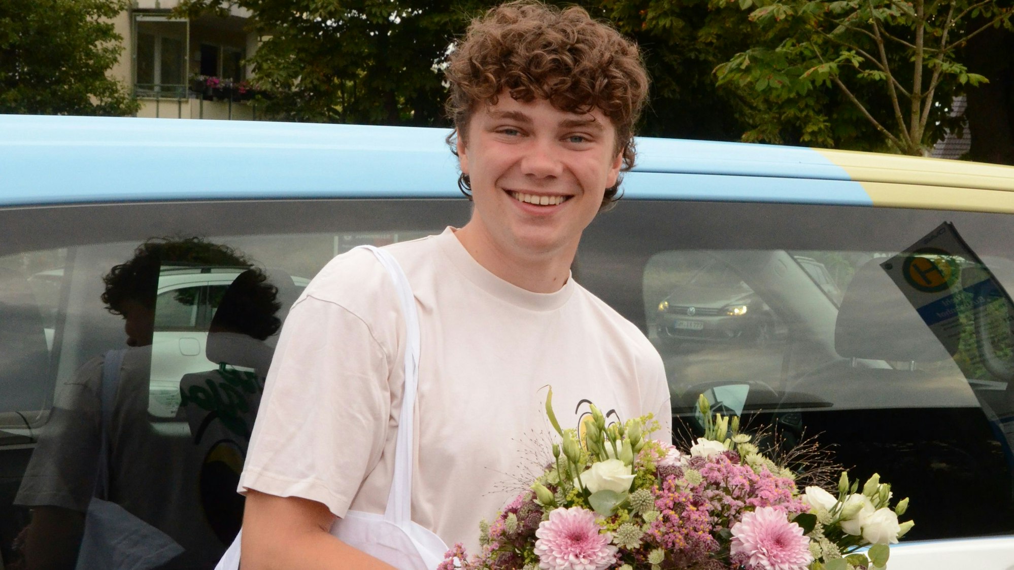 Zu sehen ist ein junger Mann mit einem Blumenstrauß in der Hand.