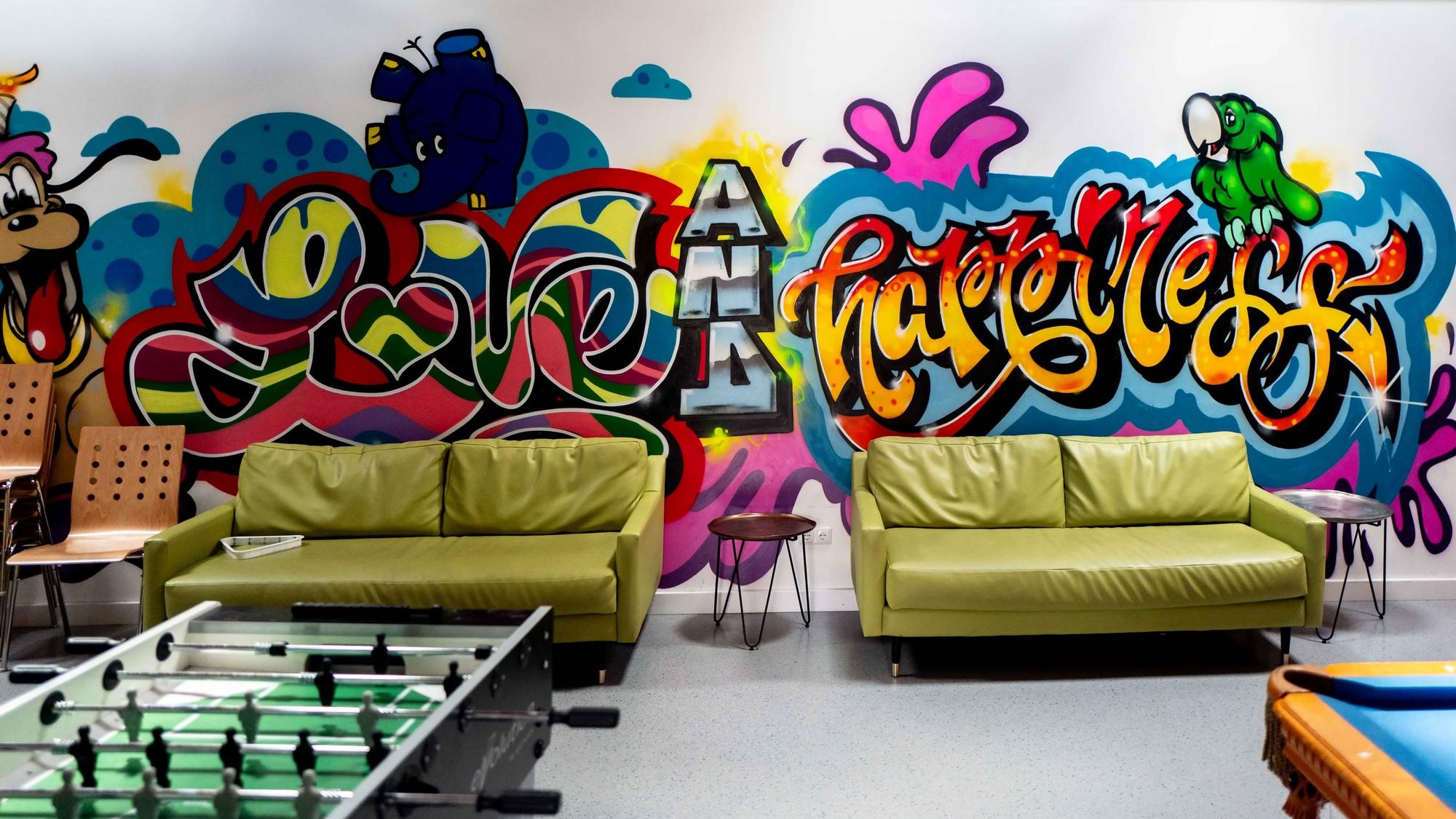 In einem Raum mit Sofas, Tischkicker und Billardtisch ist eine Wand mit Grafiti besprüht.