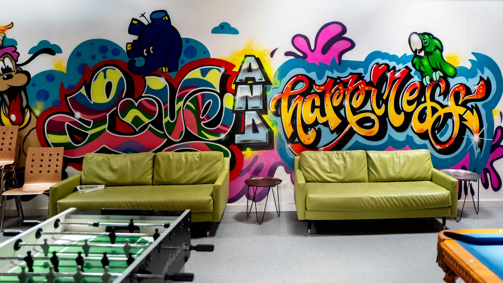 In einem Raum mit Sofas, Tischkicker und Billardtisch ist eine Wand mit Grafiti besprüht.