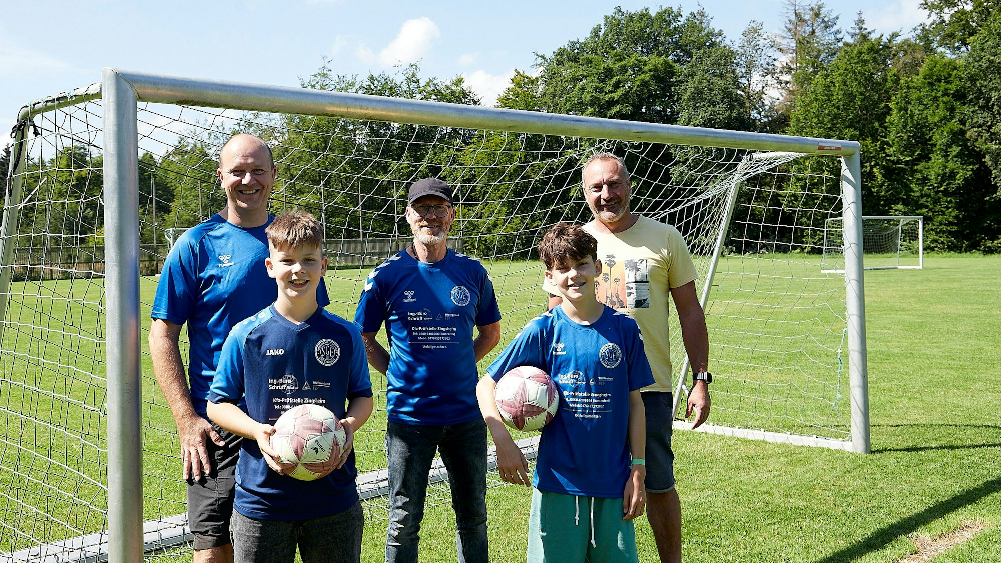 Drei Männer und zwei Jungen stehen vor einem Fußballtor.