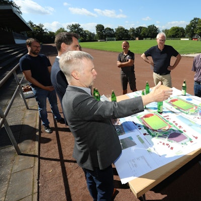Eine Gruppe vor einem Tisch mit Plänen, der im Stadion aufgestellt wurde.