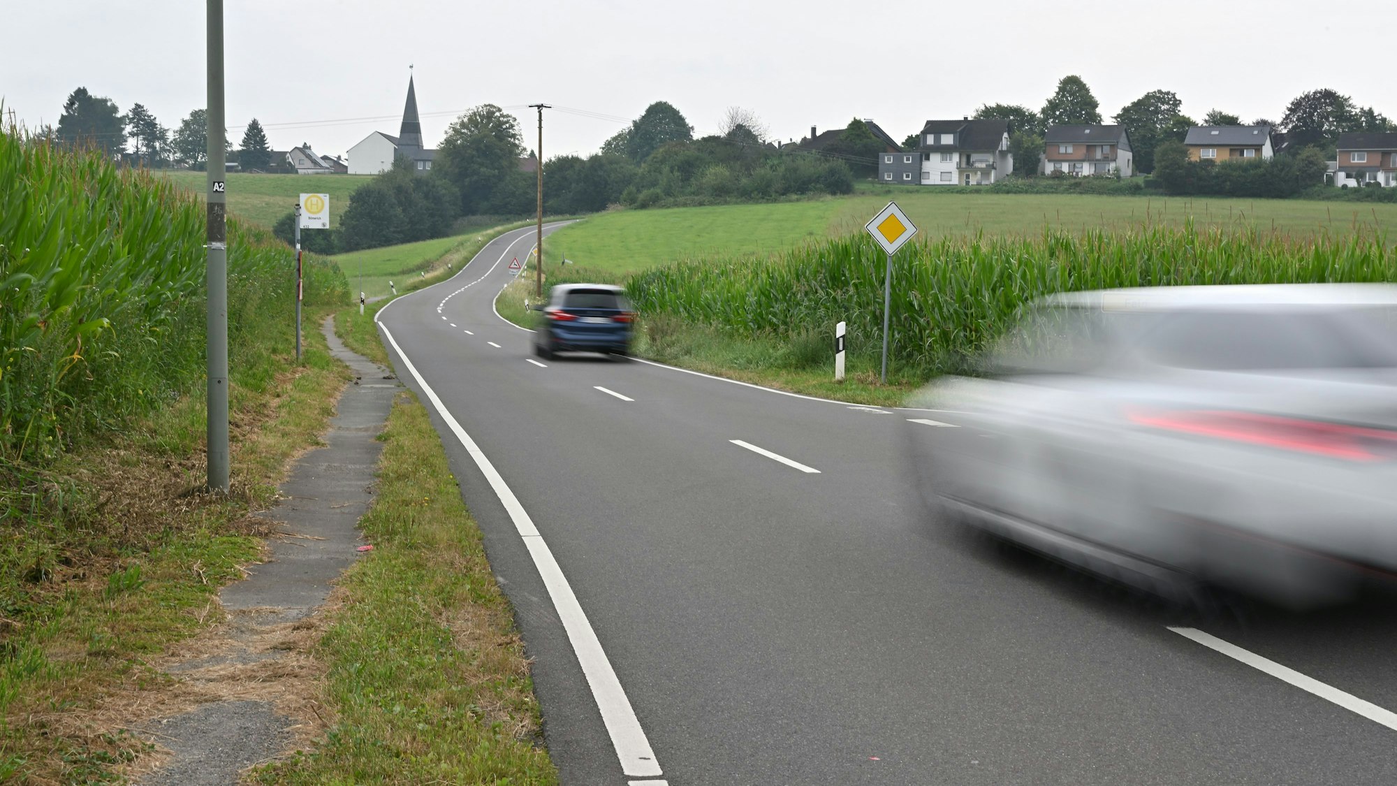 Zwei Autos fahren auf der Neschener Straße in Odenthal. Im Hintergrund die Neschener Kirche.