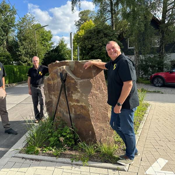 Jörg Jansen, Harald Langusch und Ulrich Gärtner stehen um eine Skulptur auf dem Dorfplatz.