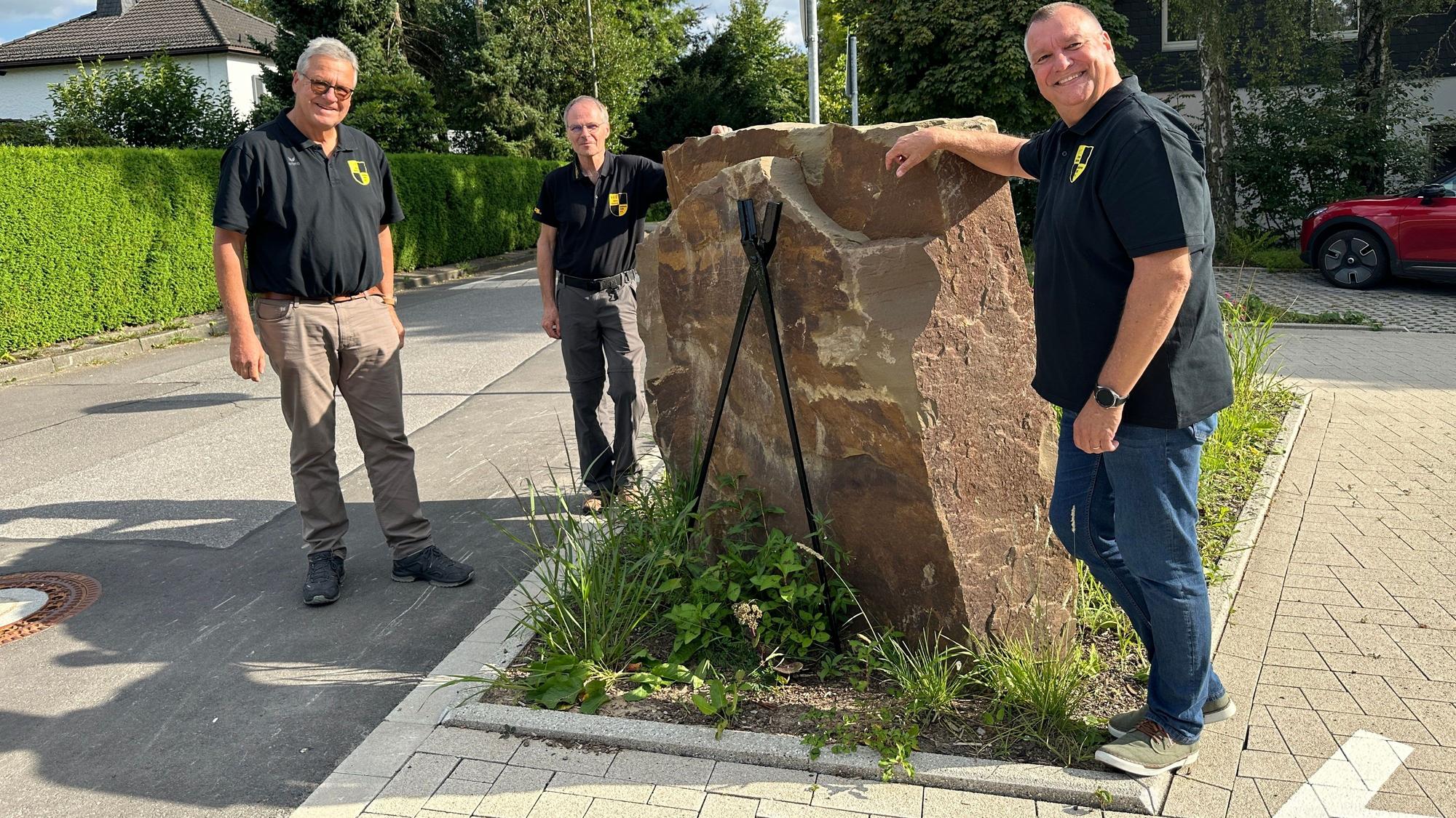 Jörg Jansen, Harald Langusch und Ulrich Gärtner stehen um eine Skulptur auf dem Dorfplatz.