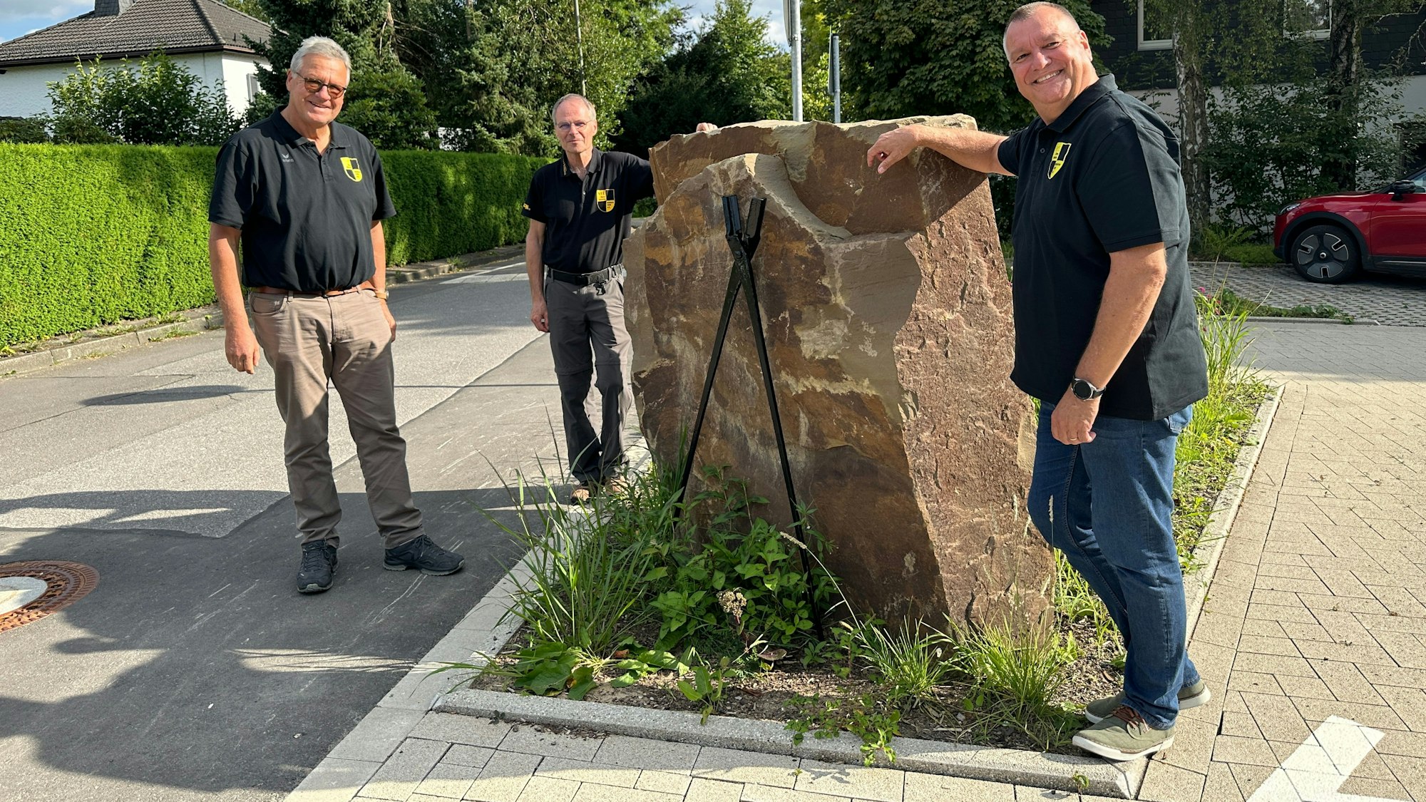 Jörg Jansen, Harald Langusch und Ulrich Gärtner stehen um eine Skulptur auf dem Dorfplatz.
