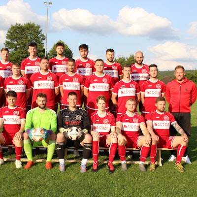 Die TuS Mechernich posiert auf einem Rasen und vor einem leicht bewölkten Himmel.