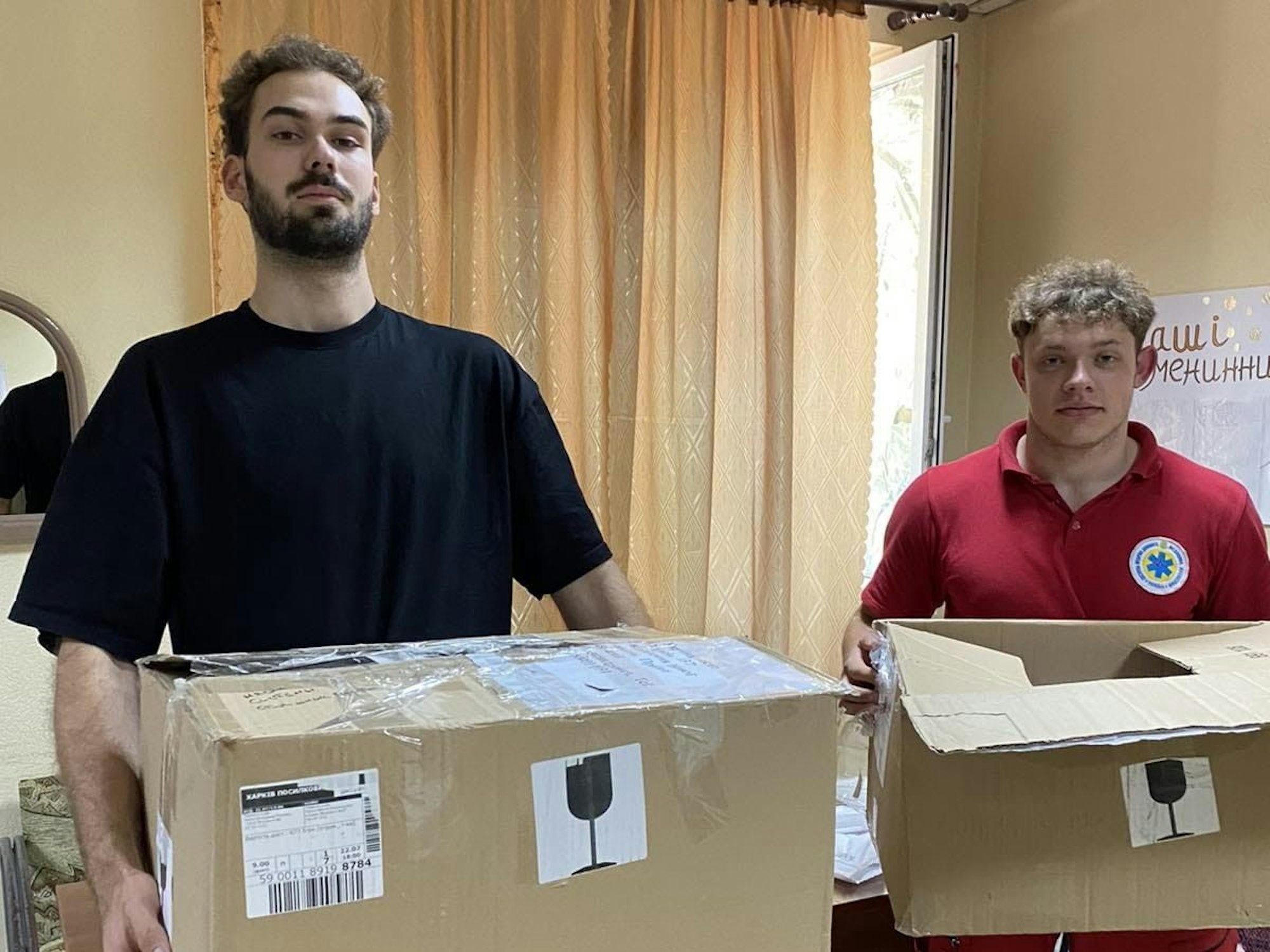 Zwei Männer in der Ukraine halten zwei Kisten mit medizinischen Hilfsmitteln in den Händen.