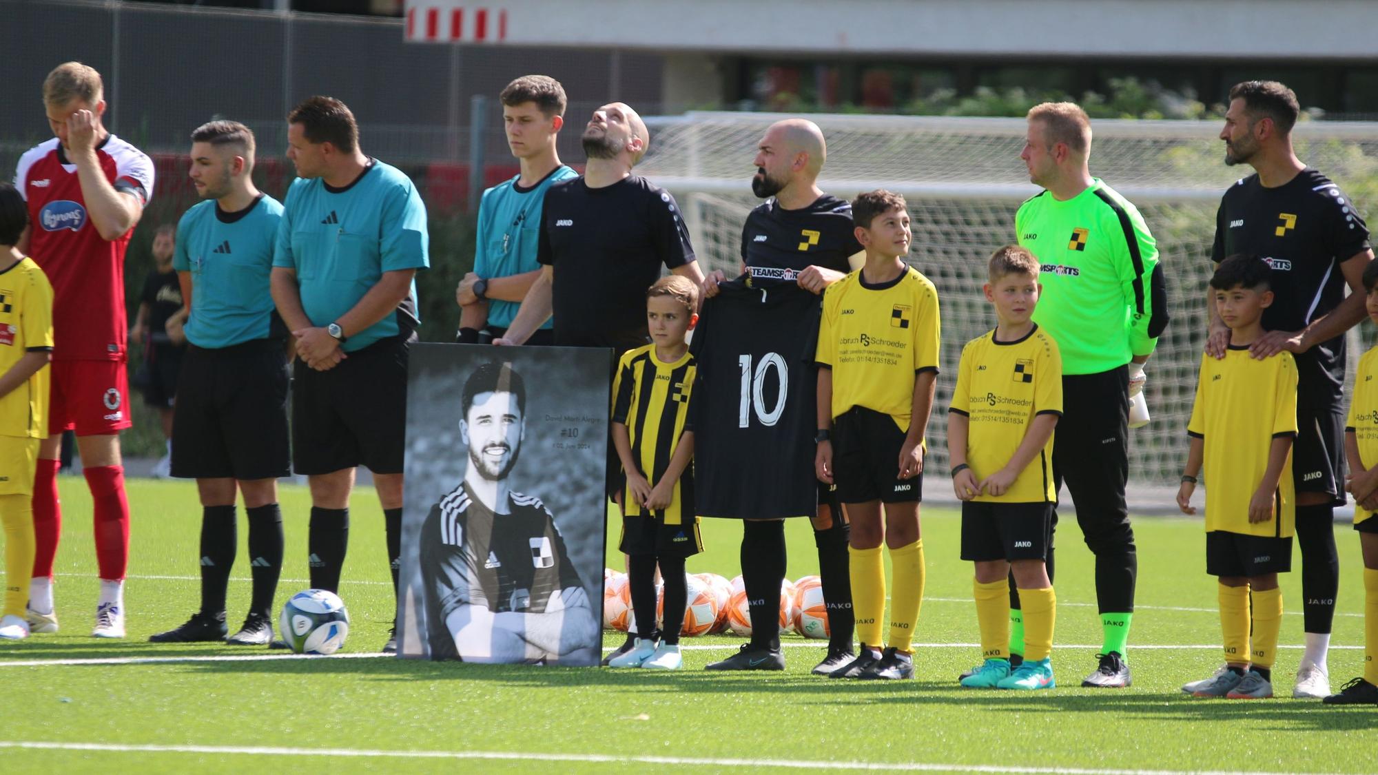 Währen einer Gedenkminute stehen die Spieler in einer Reihe, vor ihnen steht das Bild von Marti Alegre, einer von ihnen hält das Trikot mit der Nummer 10 in der Hand.