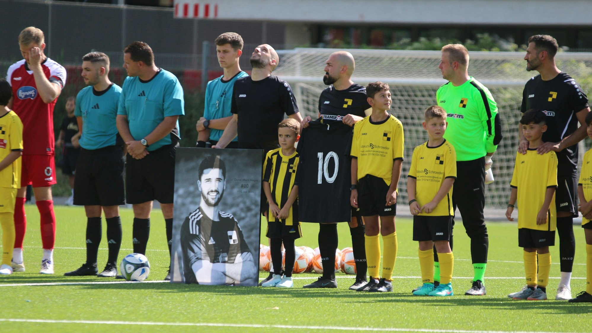 Währen einer Gedenkminute stehen die Spieler in einer Reihe, vor ihnen steht das Bild von Marti Alegre, einer von ihnen hält das Trikot mit der Nummer 10 in der Hand.
