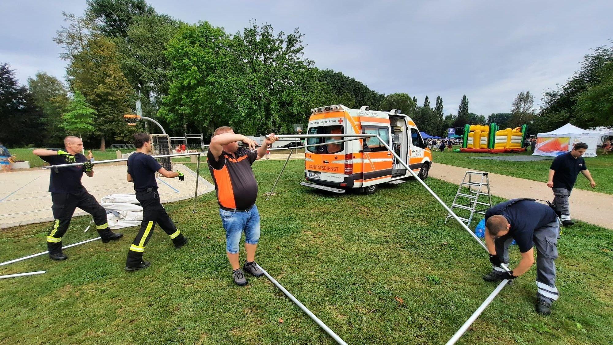 Männer bauen ein Zeltgestänge ab, im Hintergrund ein Fahrzeug des DRK