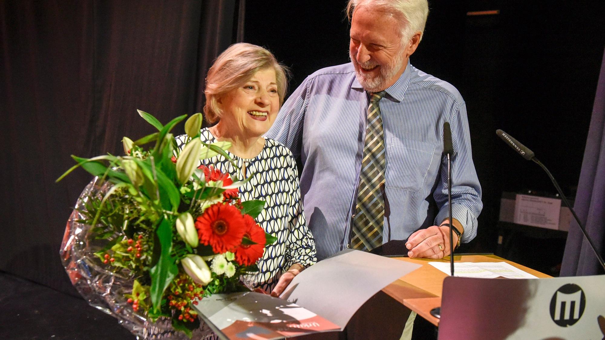 Eine Frau hält einen großen Blumenstraße in der Hand, neben ihr steht ein Man..