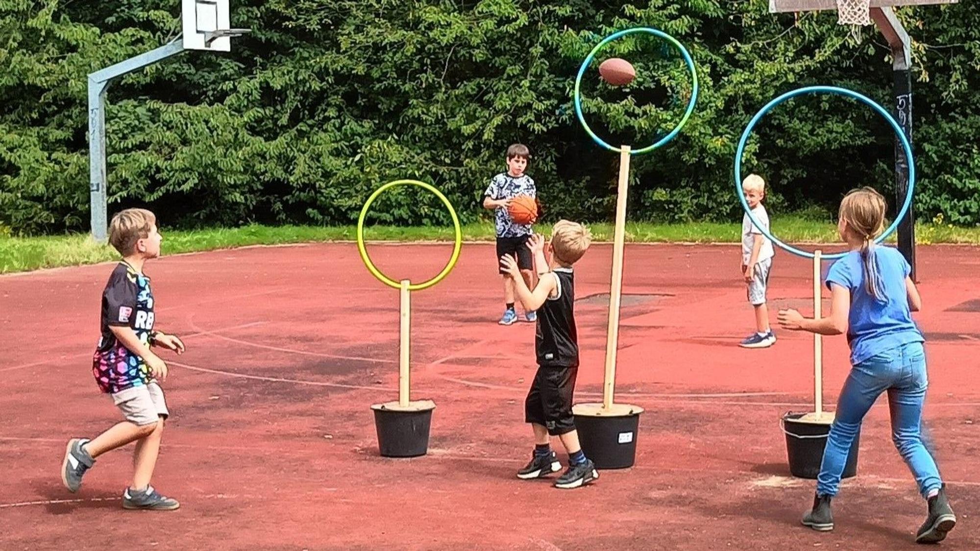 Kinder werfen Bälle durch Ringe.