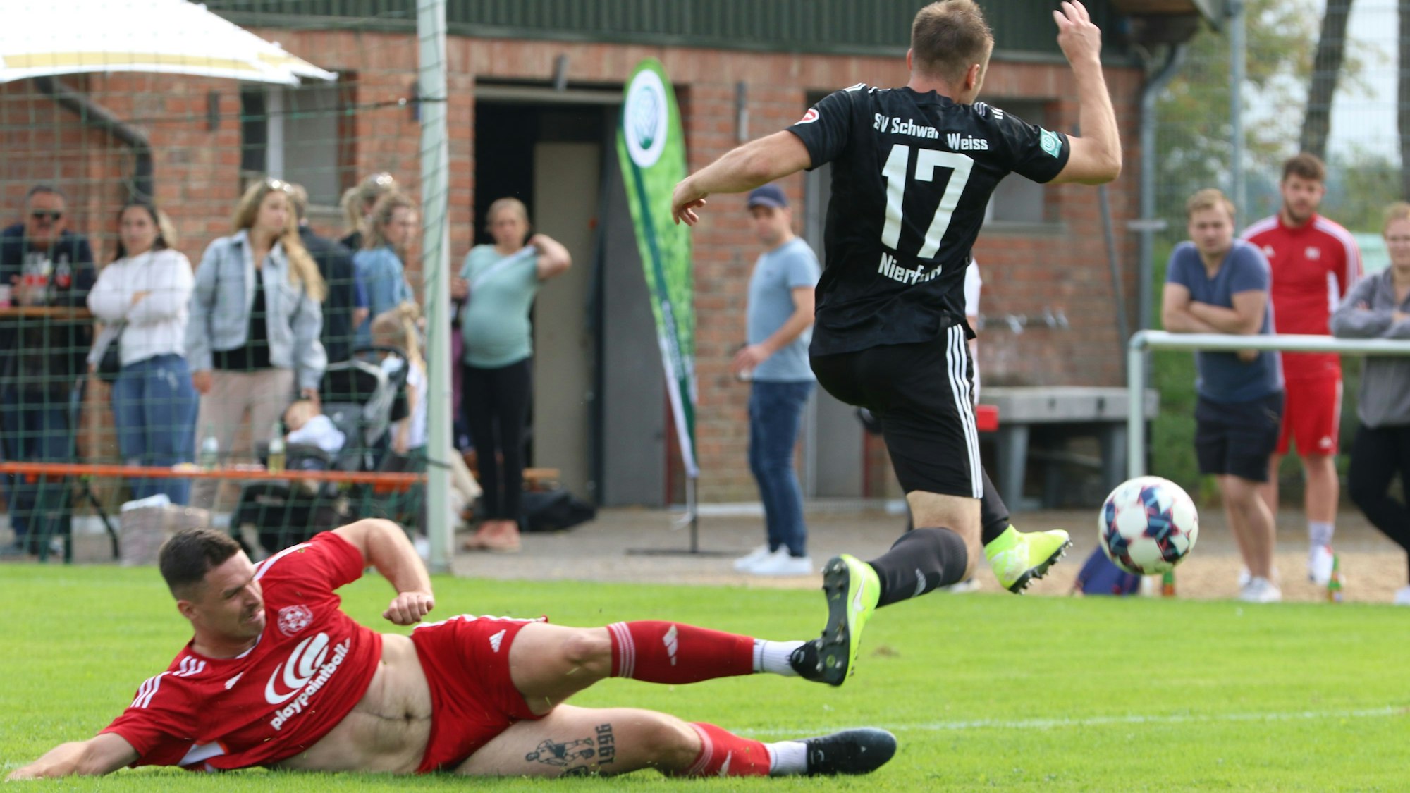 Lucas Carell grätscht, das Trikot ist ihm hochgerutscht und man sieht seinen nackten Bauch. Über die Grätsche springt Niclas Hampel hinweg.