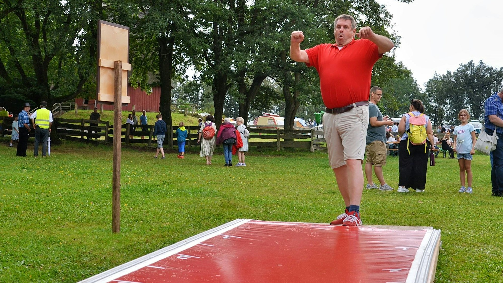 Ein Mann im roten Poloshirt und kurzer Hose versucht sich beim Kirschkernweitspucken.