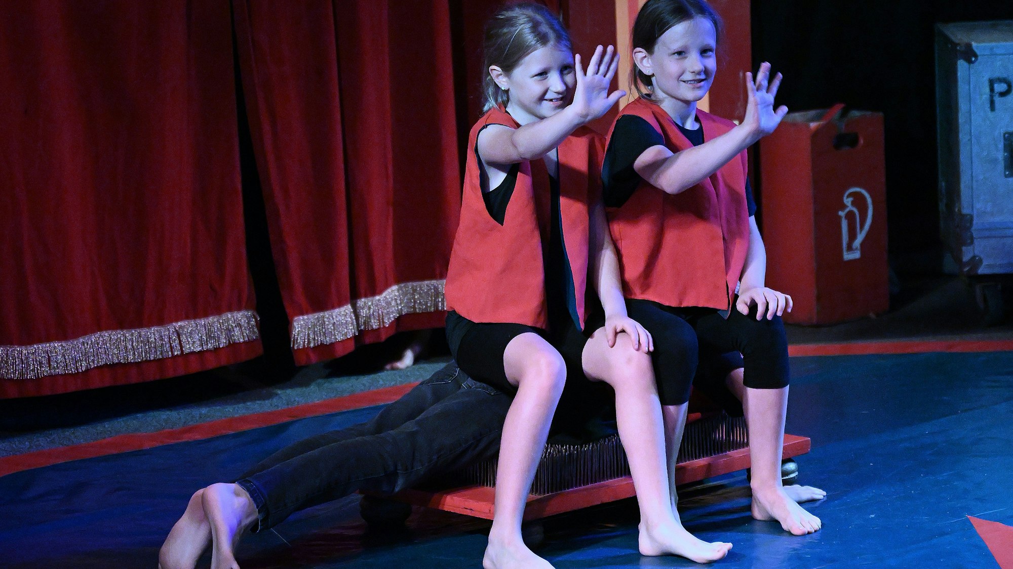 Zwei Kinder sitzen auf einem Menschen auf einem Nagelbrett und lachen.