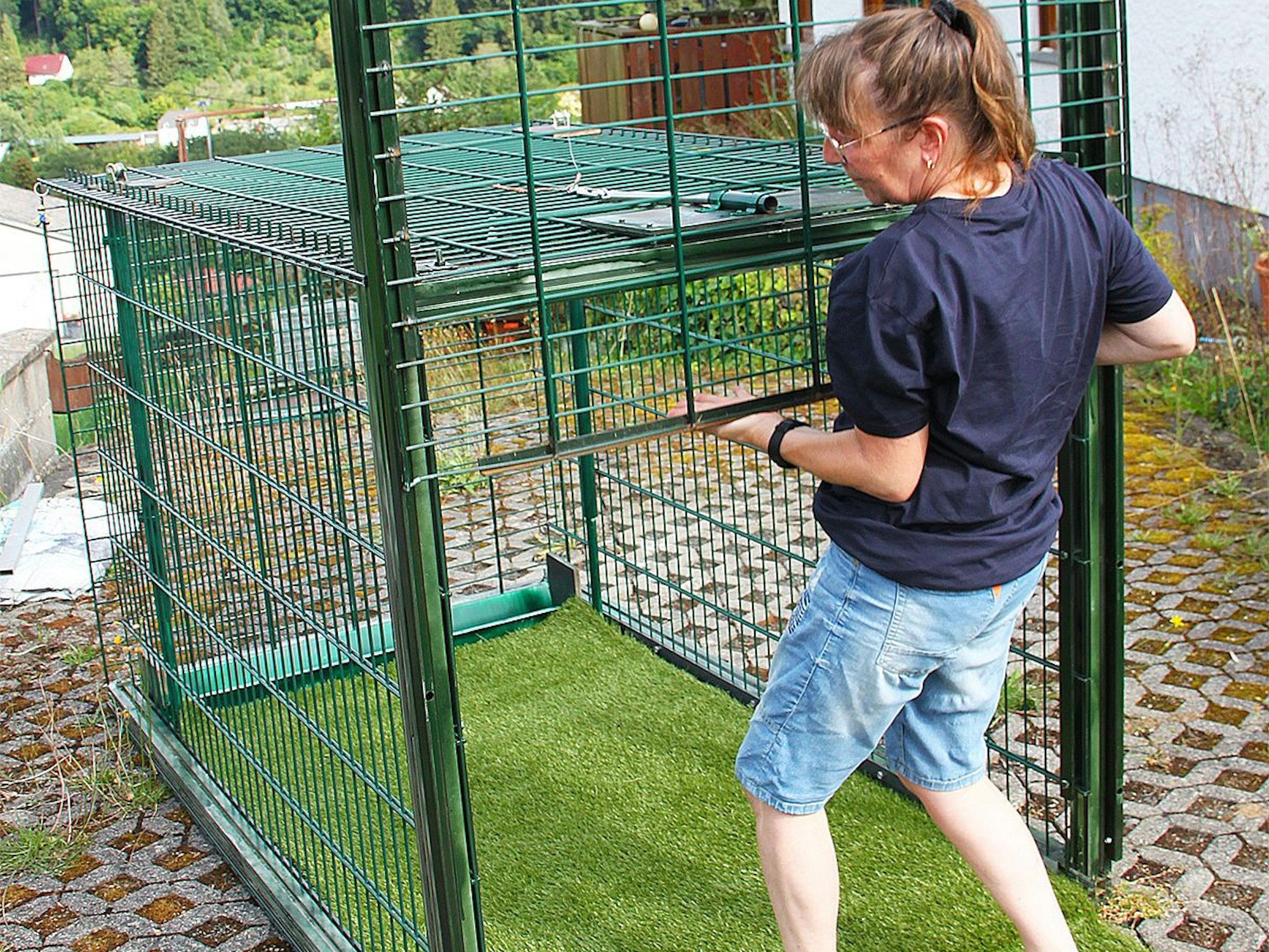 Carina Niesen hebt ein grünes Metallgitter an einem Käfig hoch. Damit öffnet sie eine Lebendfalle für große Hunde, die sie bei der Suche nach vermissten Hunden einsetzt.