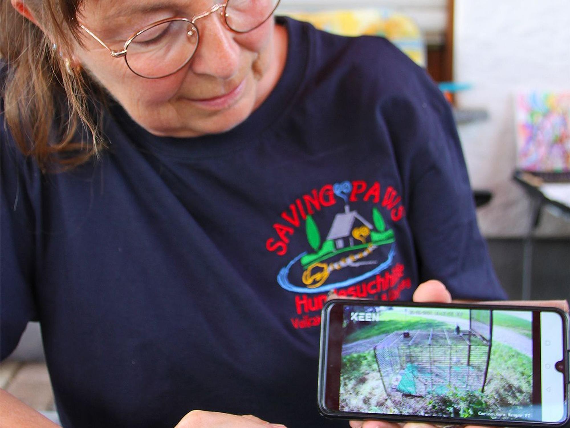 Carina Niesen hält ein Smartphone in die Kamera. Darauf ist das Bild einer Überwachungskamera zu sehen, mit dem bei einem Hunde-Sucheinsatz eine Lebendfalle beobachtet wird.