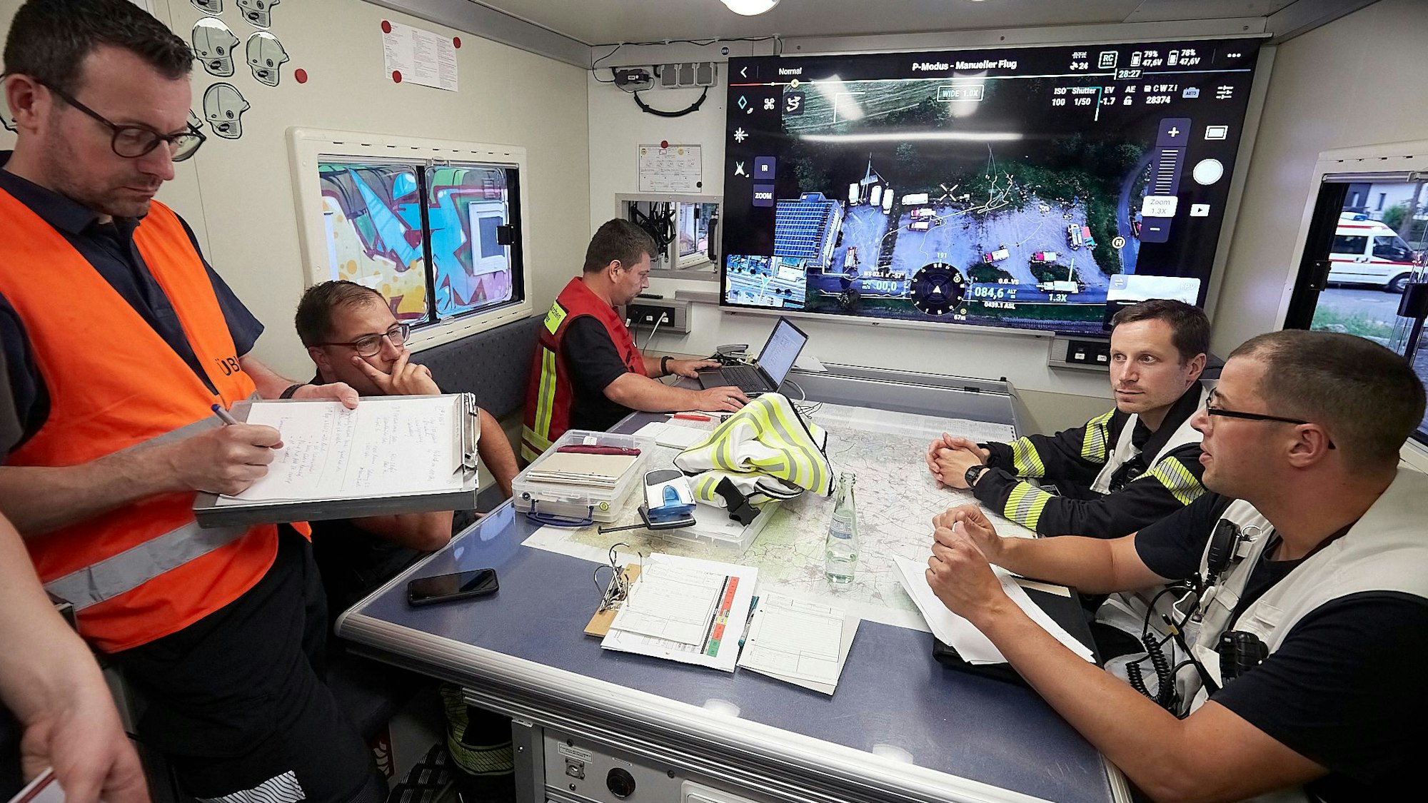 Mehrere Angehörige der Feuerwehr halten sich während der Übung im Einsatzleitwagen auf. Auf einem Großbildschirm sind Livebilder einer Drohne zu sehen.