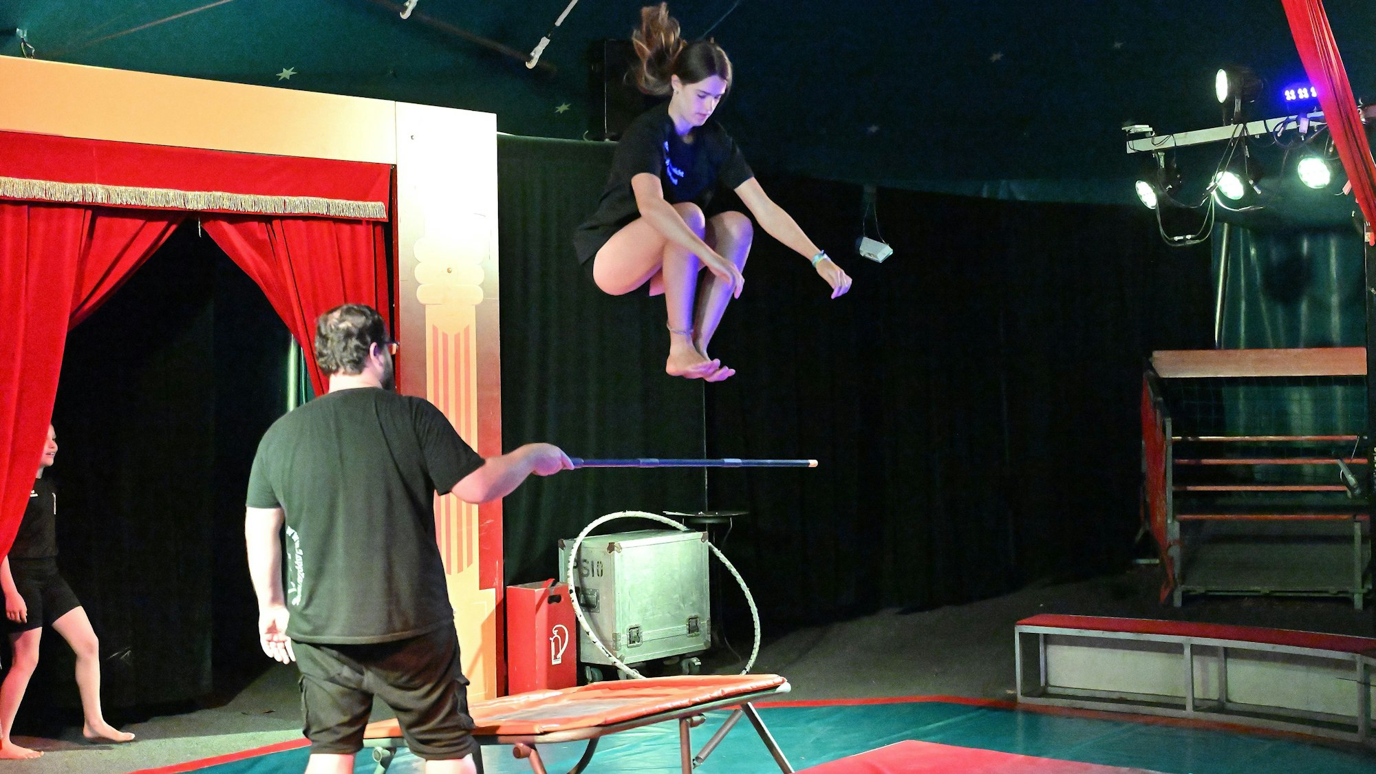 Eine Jugendliche springt mit Hilfe eines Trampolins über eine in die Luft gehaltene Stange.