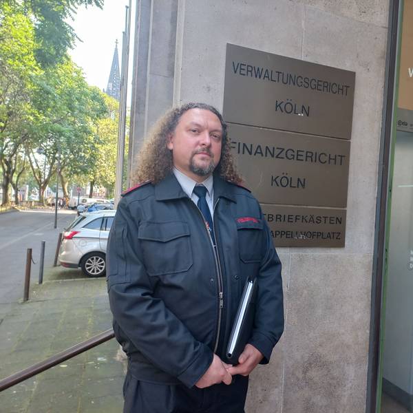 Bild eines Feuerwehrmannes in Uniform vor dem Gebäude des Kölner Verwaltungsgerichtes am Appellhofplatz
