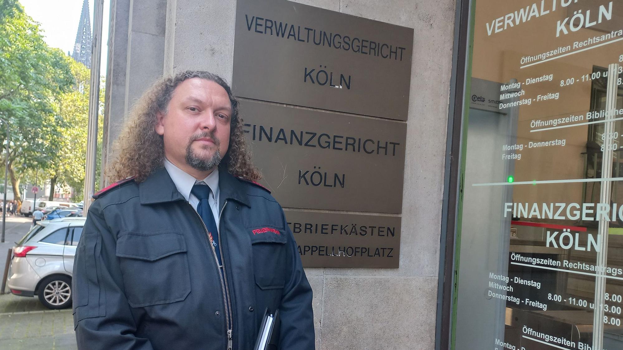 Bild eines Feuerwehrmannes in Uniform vor dem Gebäude des Kölner Verwaltungsgerichtes am Appellhofplatz