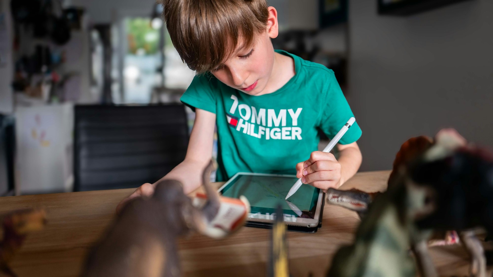 Das Bild zeigt Niilo, wie er auf einem Tablet zeichnet. Vor ihm stehen einige Dinosaurier.