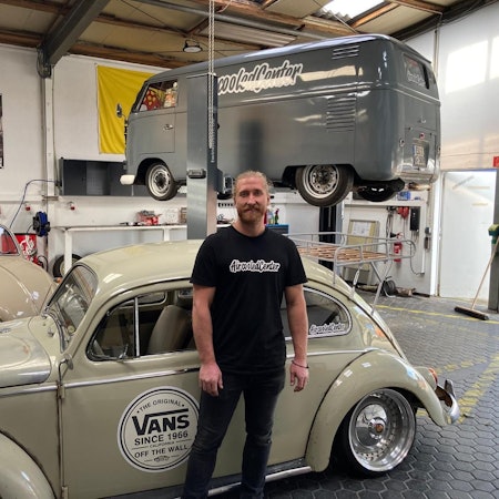 Ein Mann steht vor einem VW-Käfer in einer Werkstatt.
