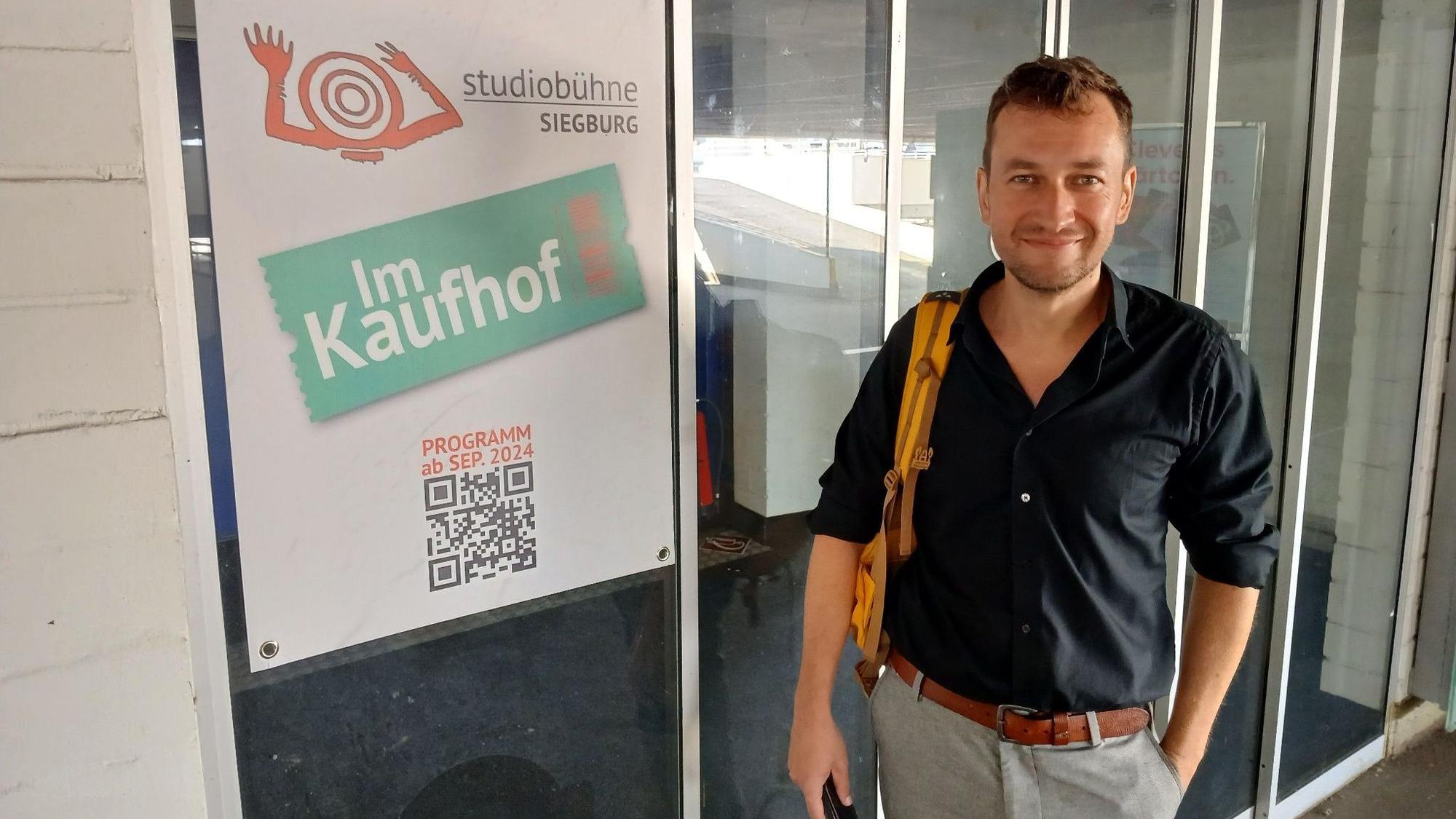 Ein Mann neben einem Plakat mit Aufschrift Studiobühne im Kaufhof