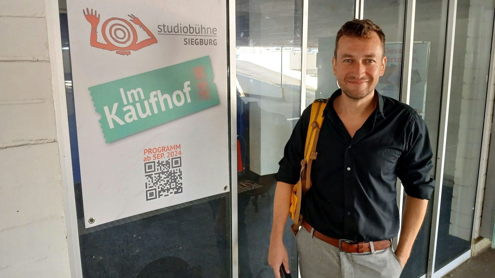 Ein Mann neben einem Plakat mit Aufschrift Studiobühne im Kaufhof