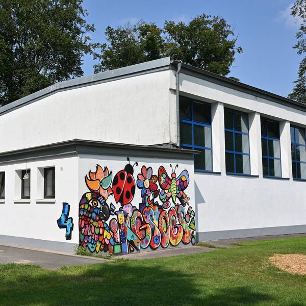 Turnhalle der Grundschule. Eine weiße Wand zeigt ein buntes Grafitto.