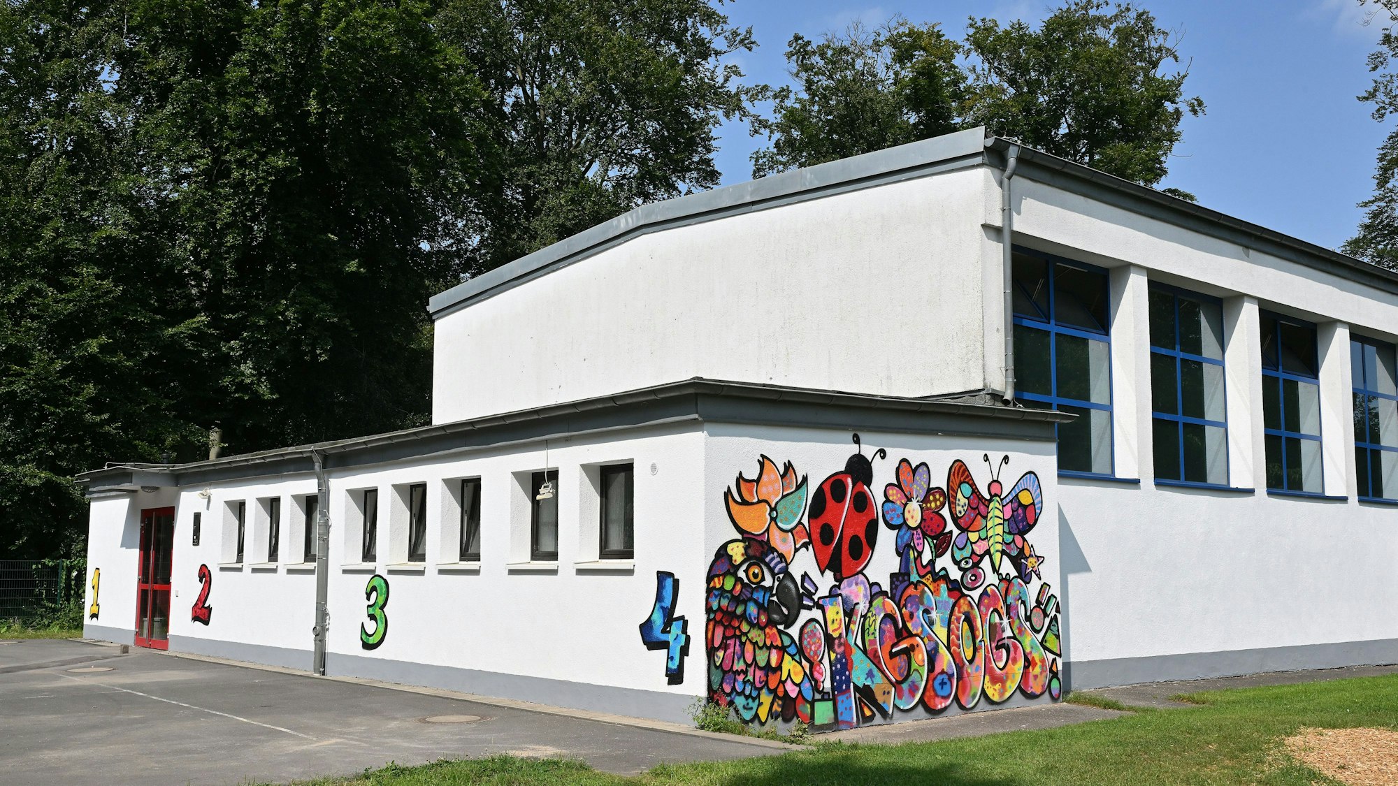 Turnhalle der Grundschule. Eine weiße Wand zeigt ein buntes Grafitto.