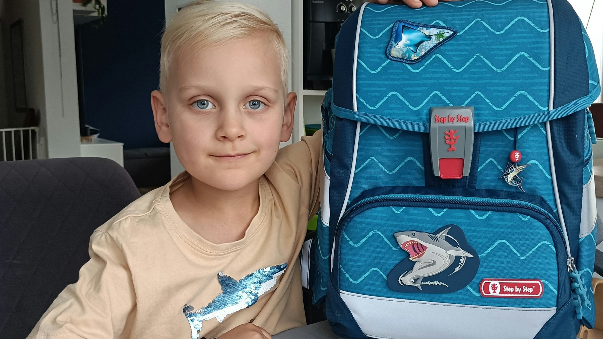 Ein Junge sitzt an einem Tisch, auf dem Tisch steht sein Schulranzen.