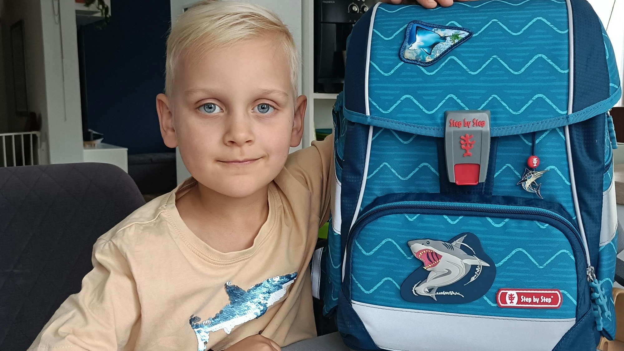 Ein Junge sitzt an einem Tisch, auf dem Tisch steht sein Schulranzen.