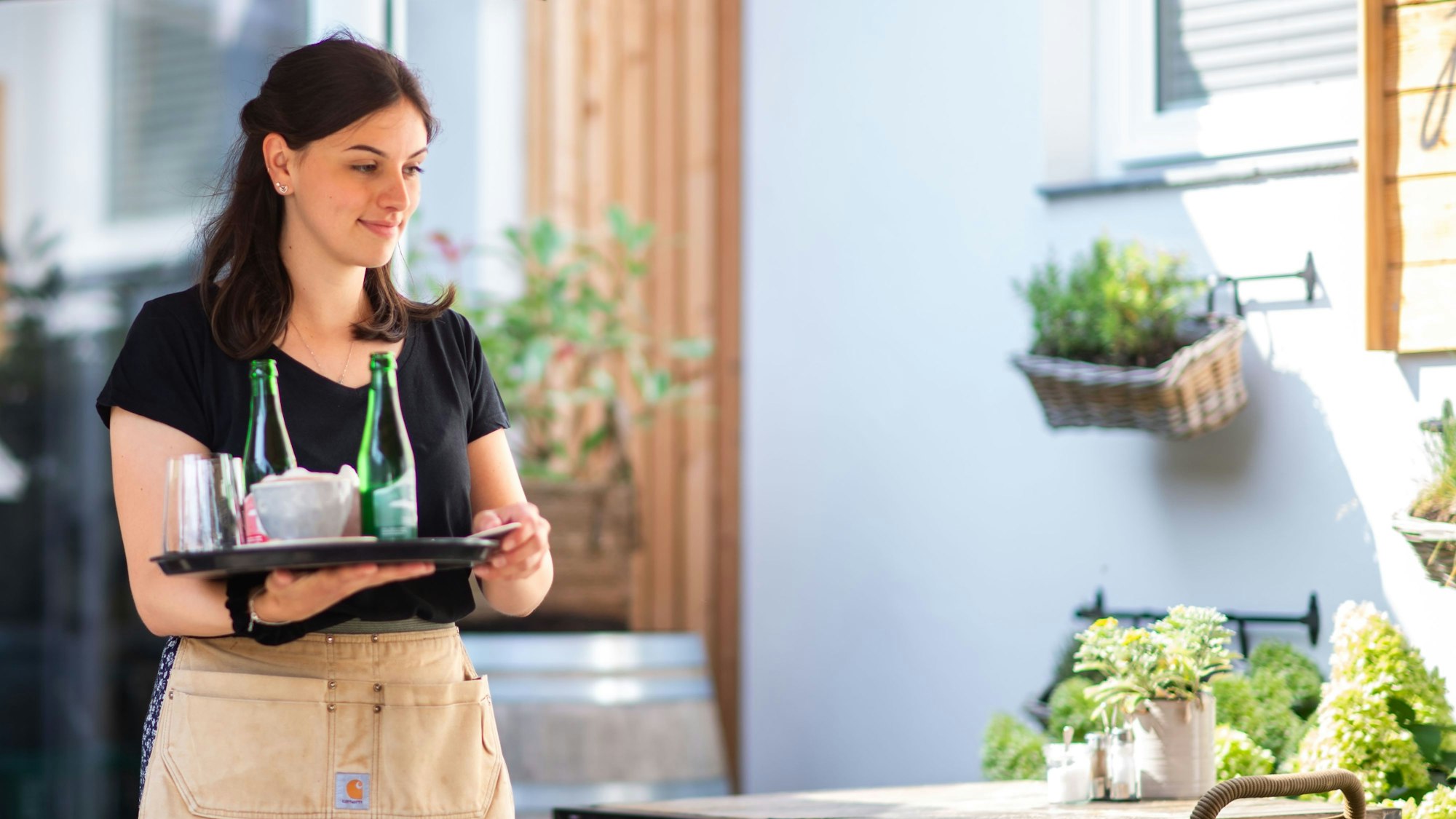 Eine Kellnerin trägt ein vollbeladenes Tablett zu einem Tisch.