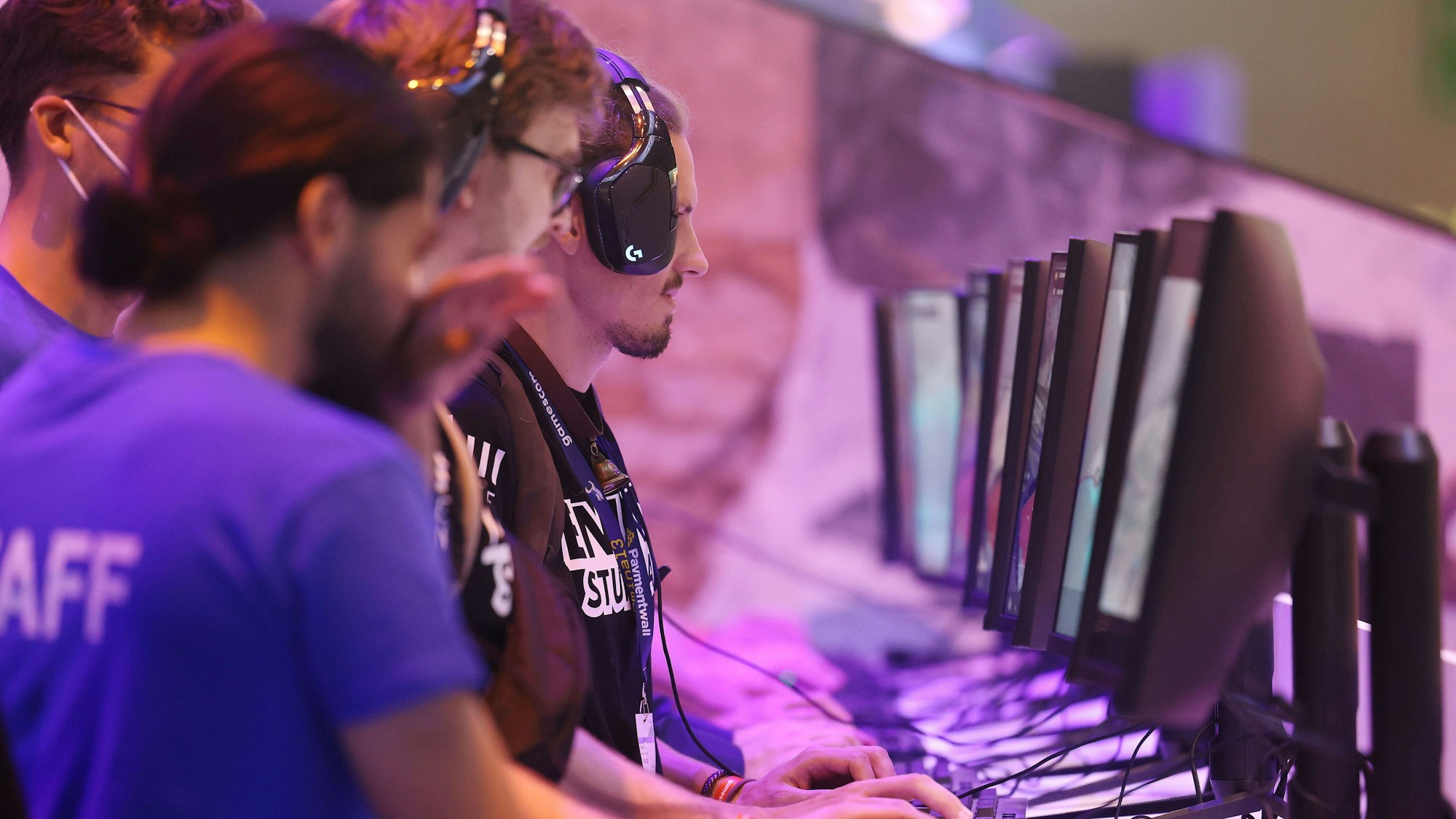 Vier Personen stehen vor Bildschirme und tragen Kopfhörer.