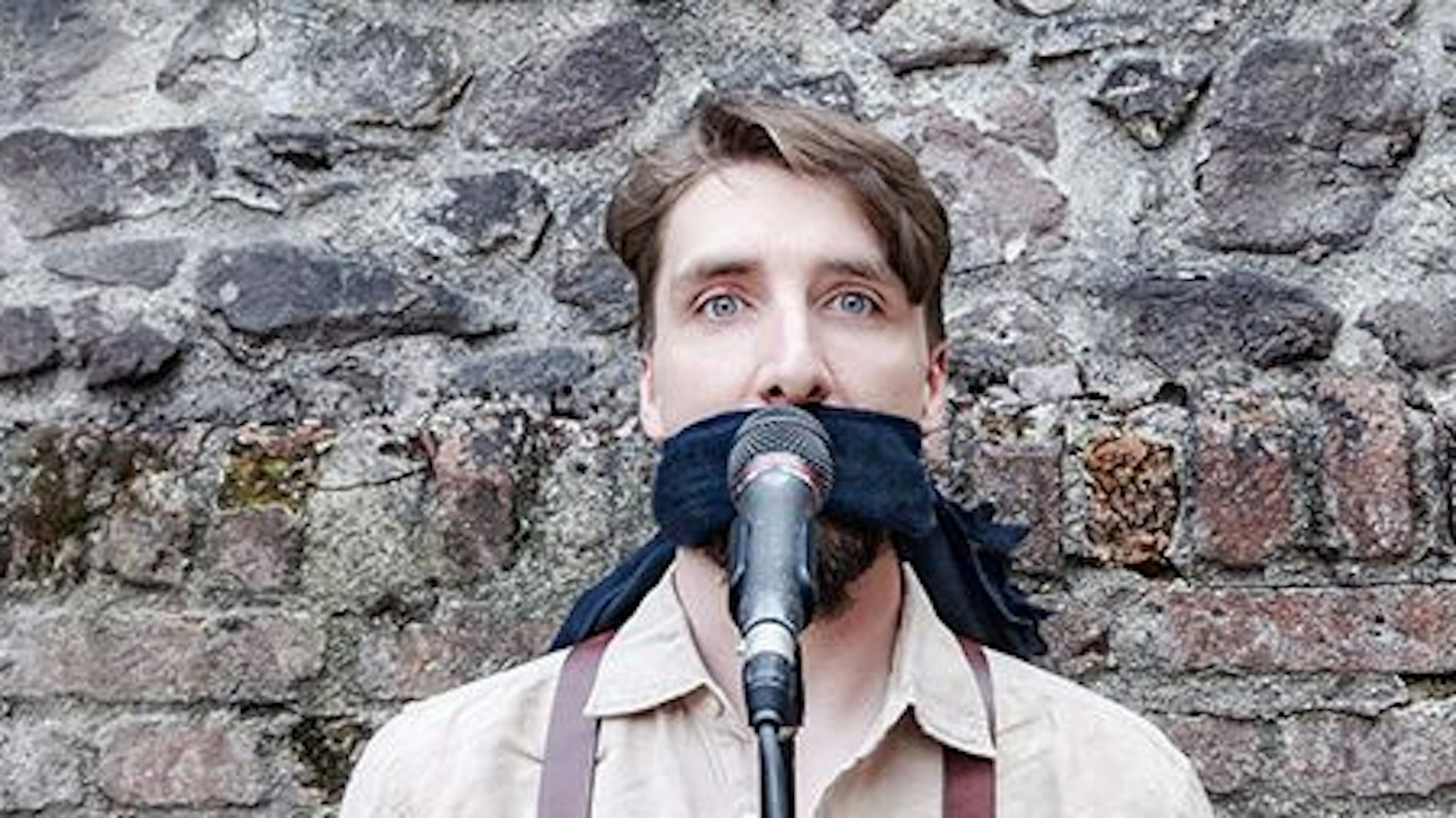 Juri von Stavenhagen hat ein Tuch über den Mund gebunden und steht hinter einen Mikrofon. .