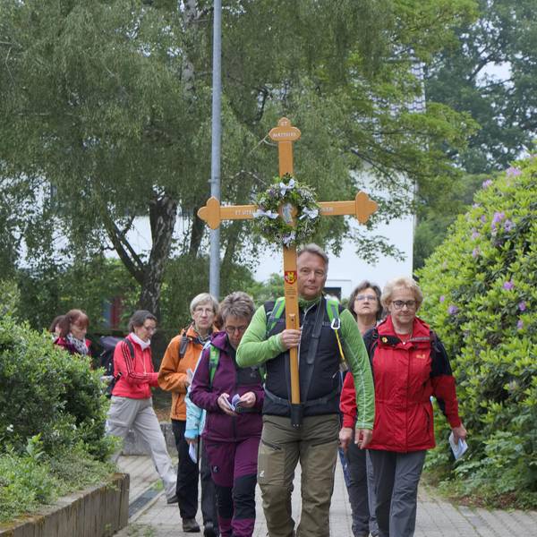 Pilgerinnen und Pilger ziehen hinter einem Mann her, der das Pilgerkreuz trägt.