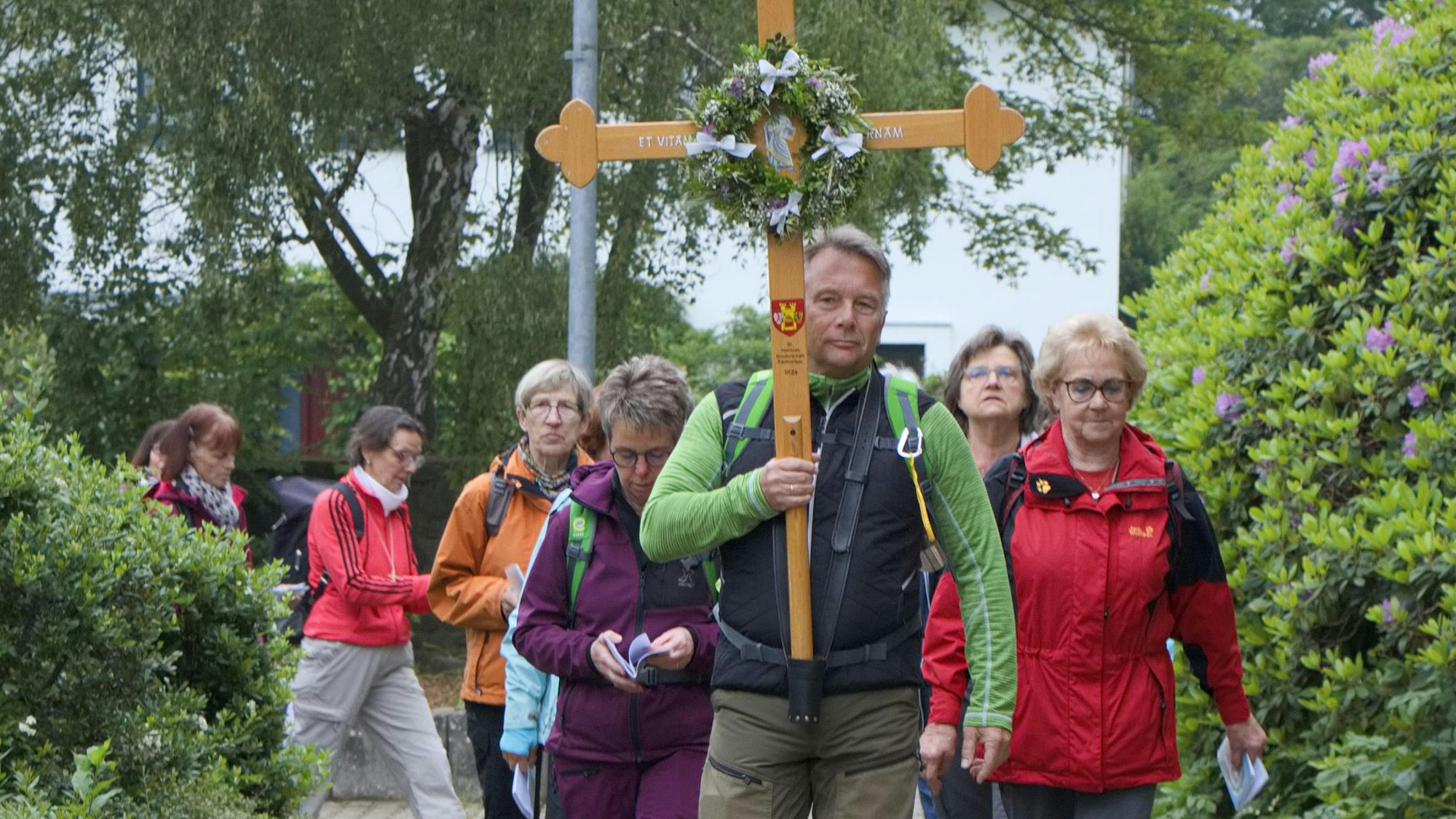 Pilgerinnen und Pilger ziehen hinter einem Mann her, der das Pilgerkreuz trägt.