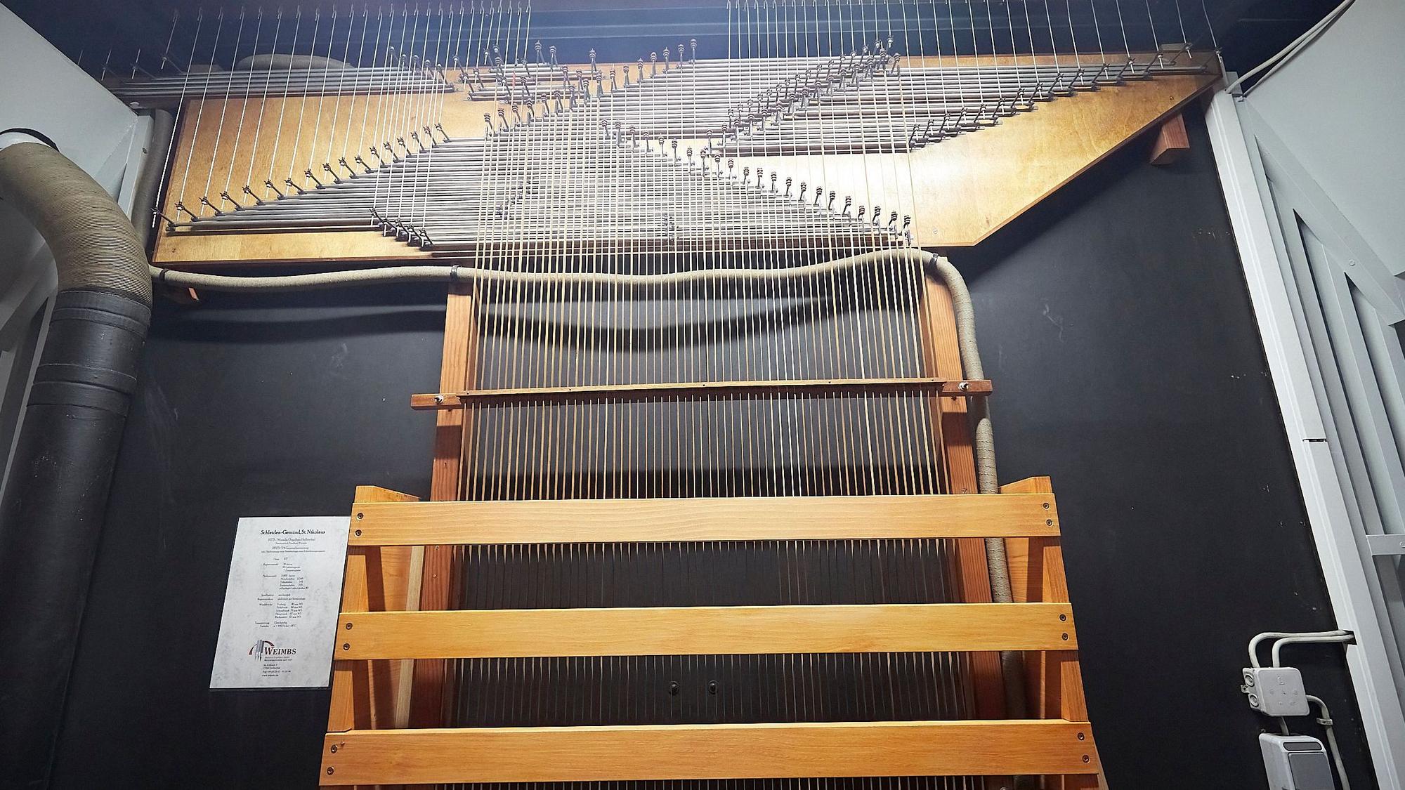 Auf dem Bild sind einige Hölzer und viele Metallstäbe vor einem dunklen Hintergrund zu sehen. Durch sie wird der Druck auf die Tasten der Orgel in Gemünd an die Orgelpfeifen übertragen.