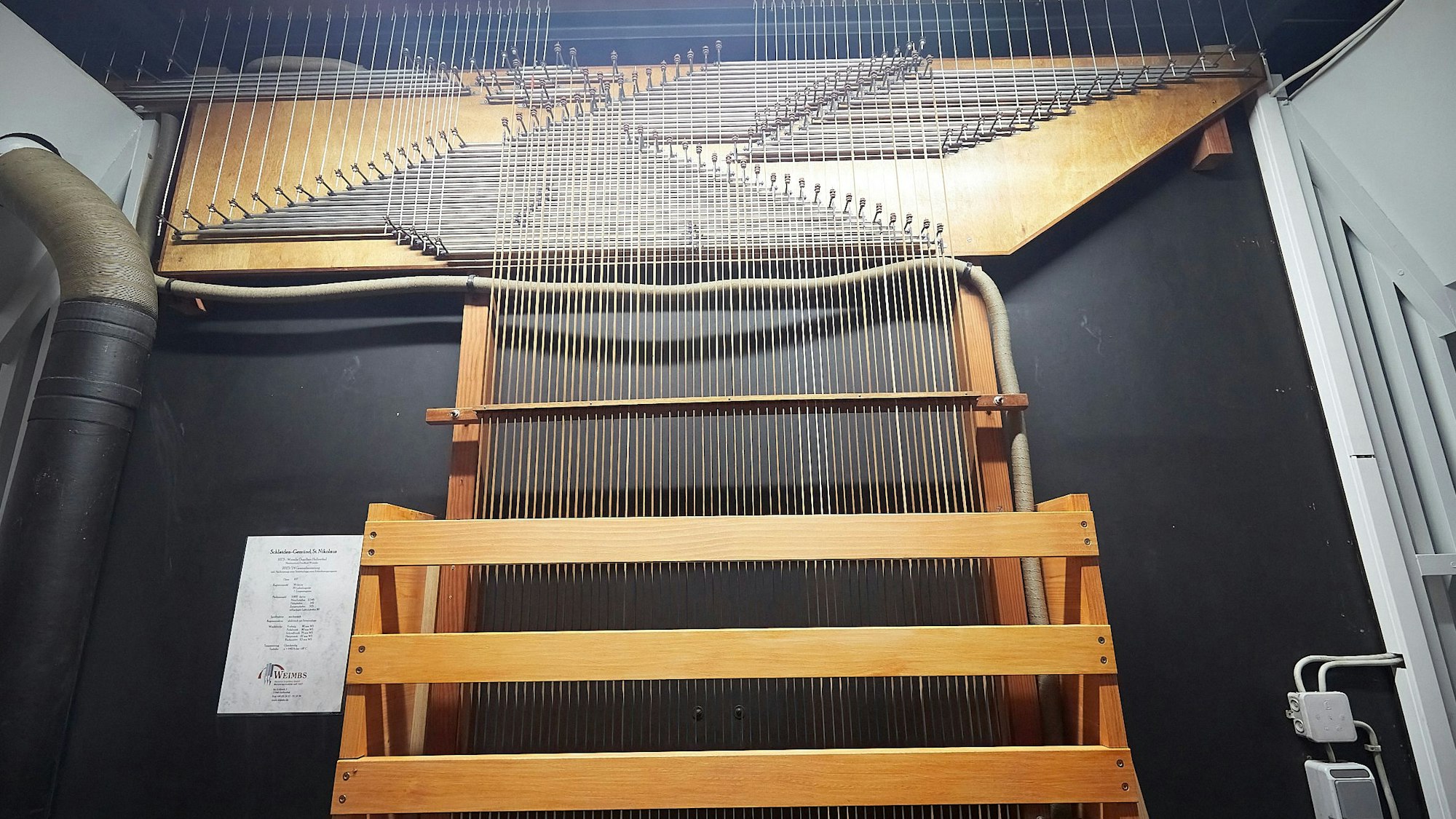 Auf dem Bild sind einige Hölzer und viele Metallstäbe vor einem dunklen Hintergrund zu sehen. Durch sie wird der Druck auf die Tasten der Orgel in Gemünd an die Orgelpfeifen übertragen.