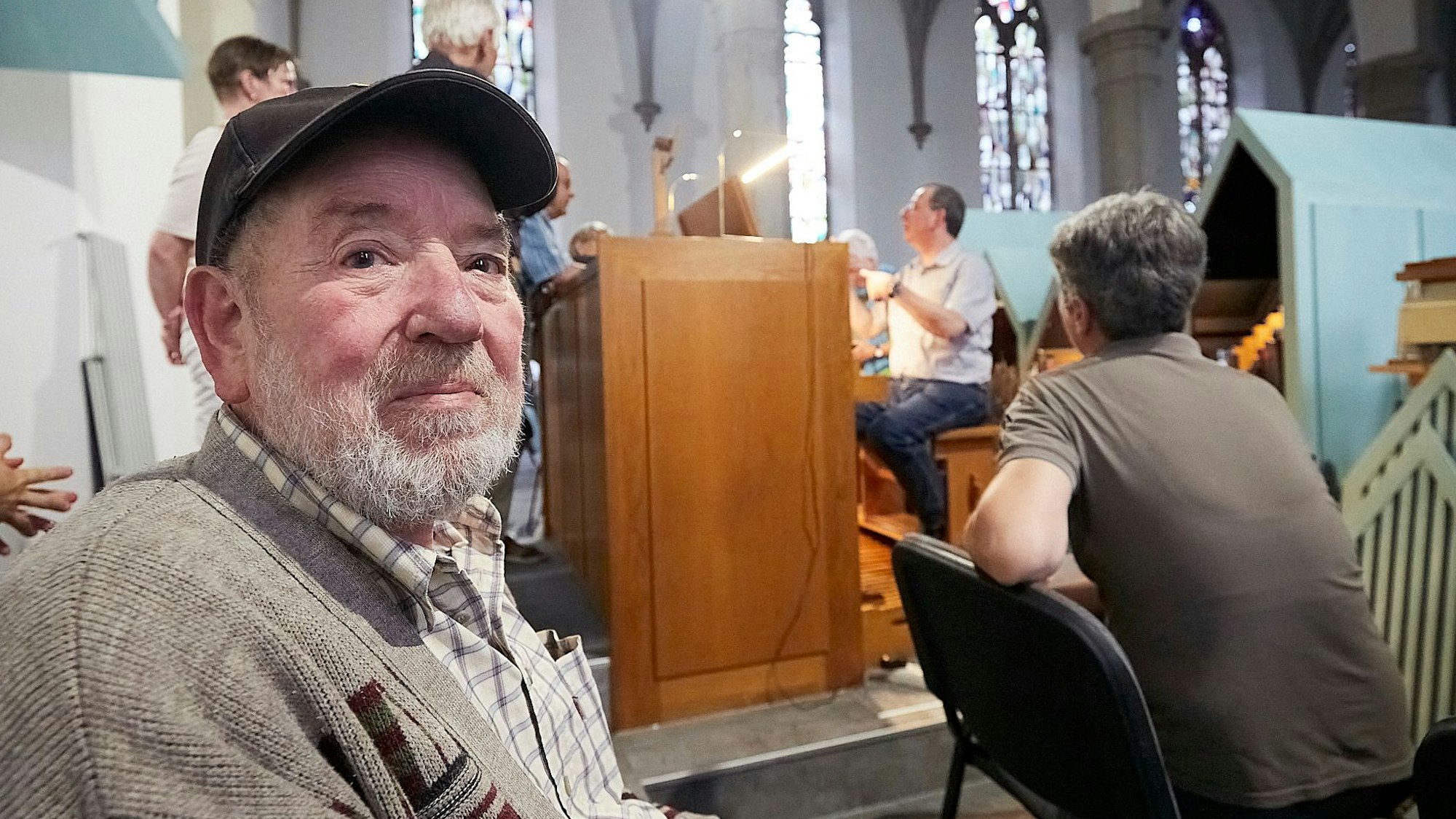 Hermann Möres sitzt vor dem Spieltisch der Orgel in der Kirche in Gemünd, an dem Organist Andreas Warler sitzt.