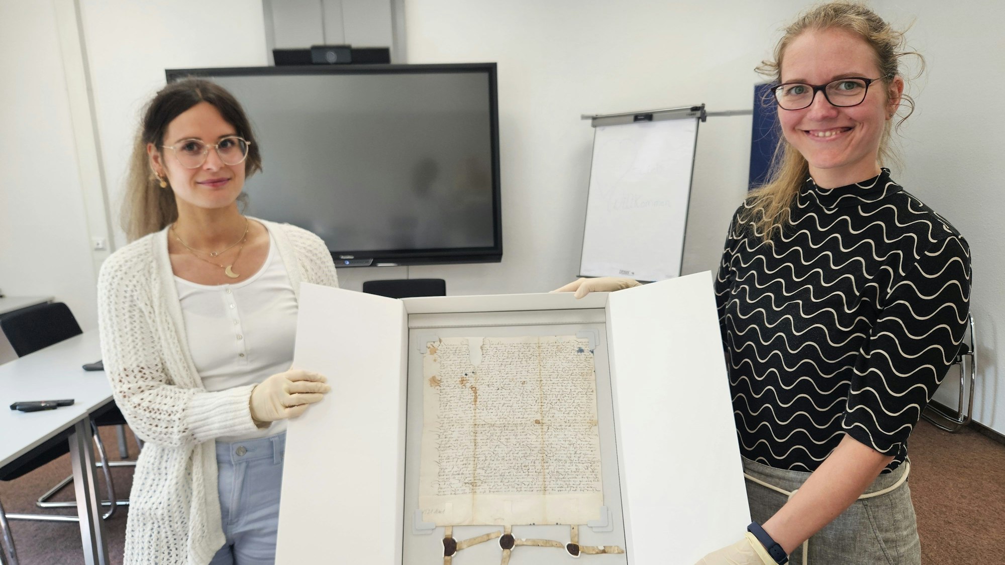 Eine Urkunde aus Schleiden aus dem Jahr 1521 präsentieren Lara Vogelsberg (l.) und Nicole Gutmann in einem Karton.