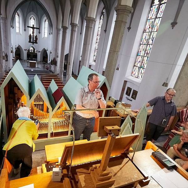 Organist Andreas Warler steht in der Mitte der Orgelempore in der Gemünder Kirche. Um ihn herum sind einige Besucher.