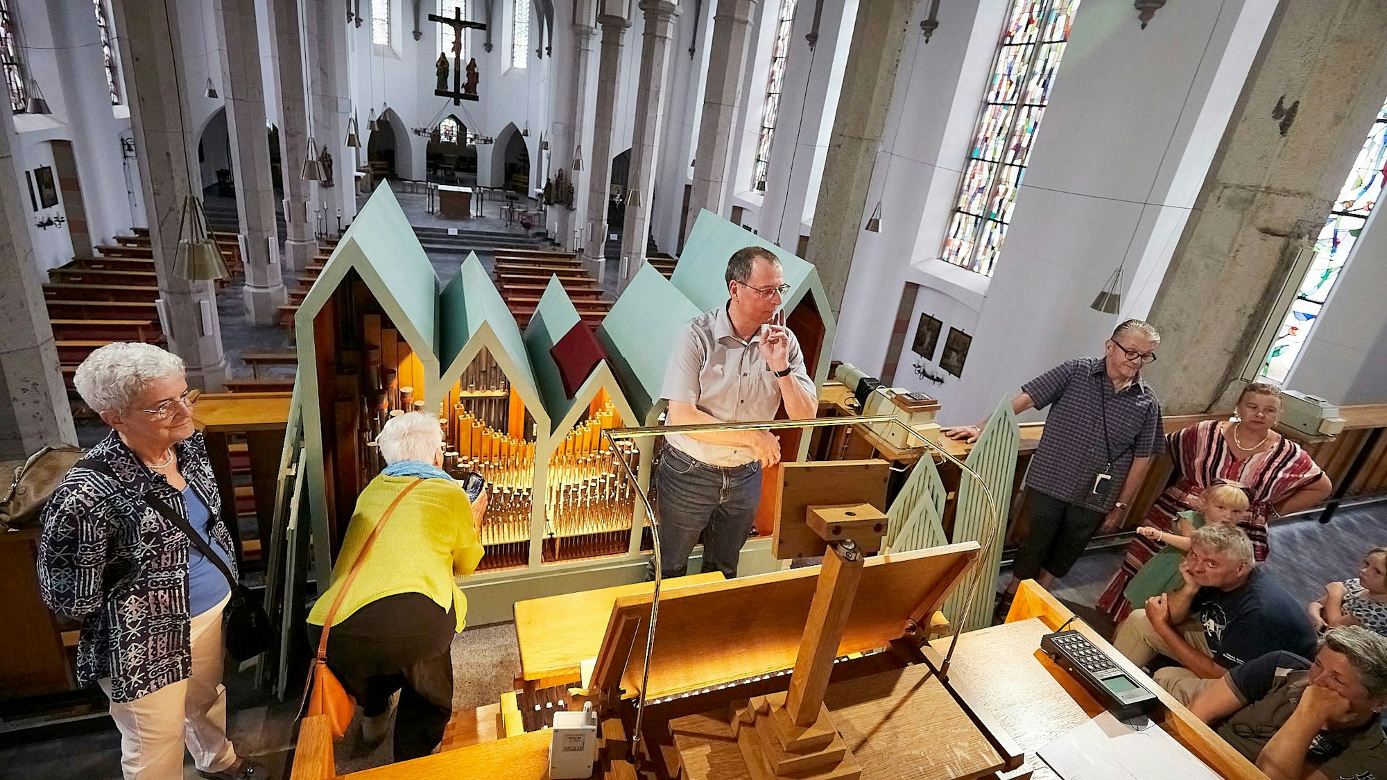 Organist Andreas Warler steht in der Mitte der Orgelempore in der Gemünder Kirche. Um ihn herum sind einige Besucher.